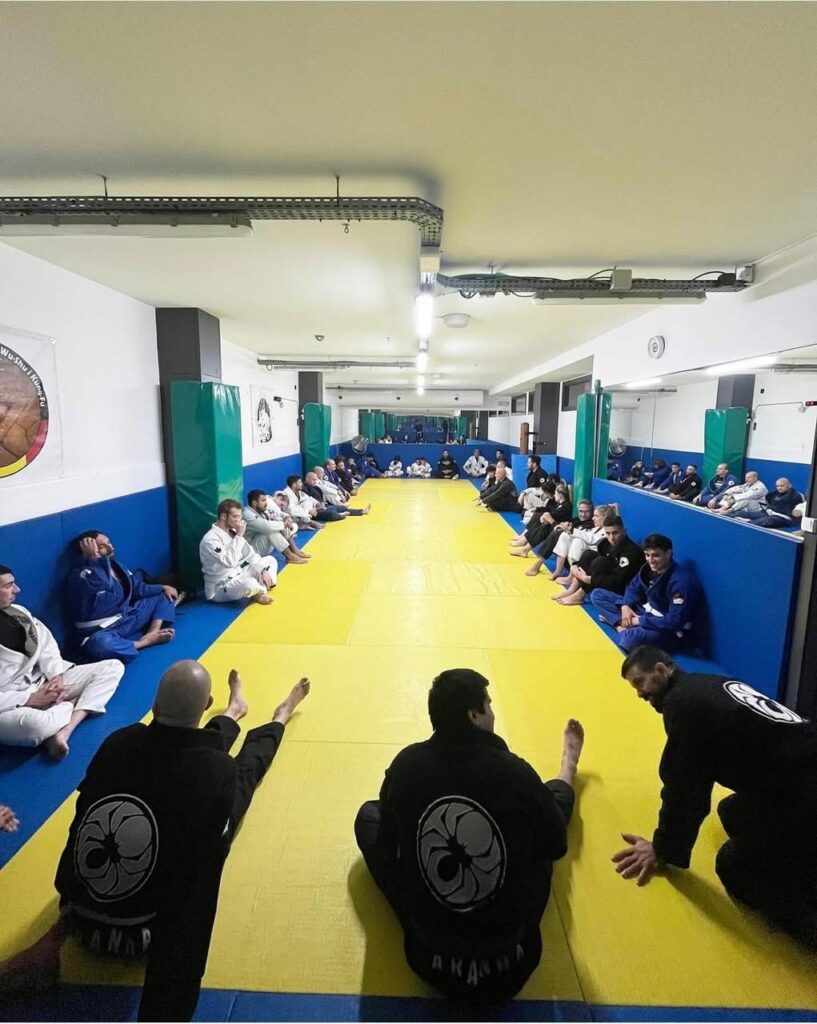 Alumnes d'Aranha Andorra amb kimono asseguts al voltant del tatami abans d'una classe de jiu-jitsu